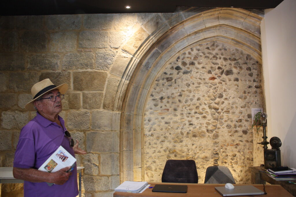 André Tandou montre un pan de mur de l'ancien couvent des Jacobins de L'Isle-en-Dodon à l'intérieur d'une agence immobilière © Récit en Série - Isabelle Desprez.